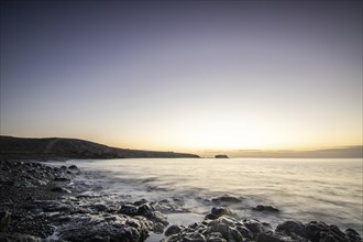 View of the sunrise over the Atlantic. View over a stone beach on a volcanic island. Cold lava