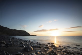 View of the sunrise over the Atlantic. View over a stone beach on a volcanic island. Cold lava