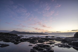 View of the sunrise over the Atlantic. Dreamlike clouds and a bay with a stone beach on a volcanic