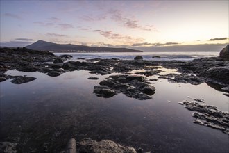 View of the sunrise over the Atlantic. Dreamlike clouds and a bay with a stone beach on a volcanic