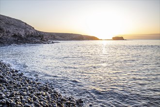 View of the sunrise over the Atlantic. View over a stone beach on a volcanic island. Cold lava