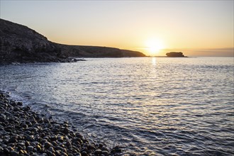 View of the sunrise over the Atlantic. View over a stone beach on a volcanic island. Cold lava