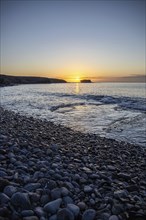 View of the sunrise over the Atlantic. View over a stone beach on a volcanic island. Cold lava