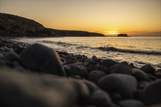 View of the sunrise over the Atlantic. View over a stone beach on a volcanic island. Cold lava