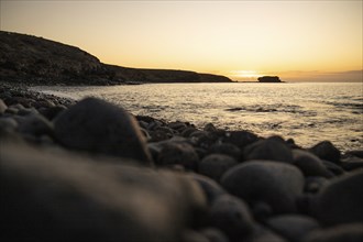 View of the sunrise over the Atlantic. View over a stone beach on a volcanic island. Cold lava