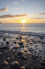 View of the sunrise over the Atlantic. View over a stone beach on a volcanic island. Cold lava