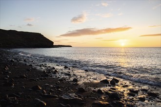 View of the sunrise over the Atlantic. View over a stone beach on a volcanic island. Cold lava