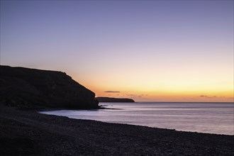 View of the sunrise over the Atlantic. A coastline and a bay with a rocky beach on a volcanic