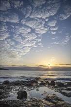 View of the sunrise over the Atlantic. Dreamlike clouds and a bay with a stone beach on a volcanic