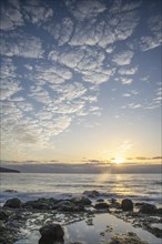 View of the sunrise over the Atlantic. Dreamlike clouds and a bay with a stone beach on a volcanic