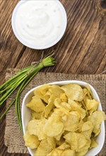 Potato Chips (Sour Cream taste) on rustic wooden background (close-up shot)