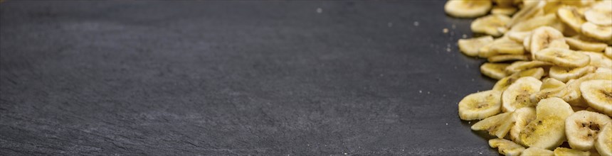 Some Dried Banana Chips on a slate slab as detailed close-up shot, selective focus