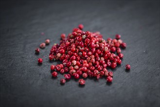 Portion of Pink Peppercorns as detailed close up shot on a slate slab, selective focus