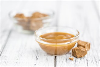 Caramel Sauce as high detailed close-up shot on a vintage wooden table (selective focus)