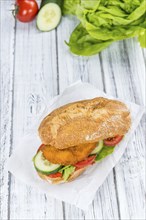 Bun with a Chicken Schnitzel on wooden background (close-up shot, selective focus)