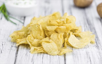 Potato Chips (Sour Cream taste) on rustic wooden background (close-up shot)