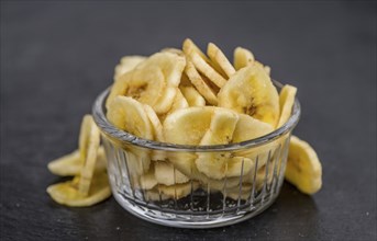 Some Dried Banana Chips on a slate slab as detailed close-up shot, selective focus