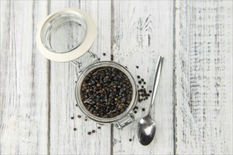 Wooden table with preserved black Peppercorns, selective focus, close-up shot