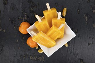 Homemade Tangerine Popsicles with some fresh fruits (close-up shot) on a vintage background