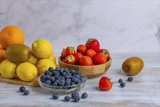 Arrangement of fresh strawberries, lemons, oranges, kiwis and blueberries on wood against a marble