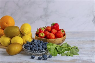 Arrangement of fresh strawberries, lemons, oranges, kiwis and blueberries on wood against a marble