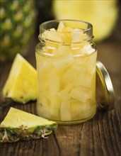 Chopped Pineapple (preserved) as high detailed close-up shot on a vintage wooden table, selective