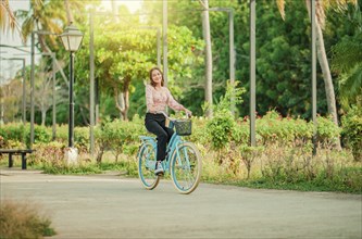 Happy girl riding a bicycle in a park at sunset. Portrait of smiling young woman riding a bicycle