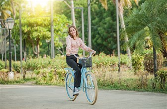 Portrait of smiling young woman riding a bicycle in a nice park. Happy girl riding a bicycle in a