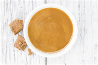 Caramel Sauce as high detailed close-up shot on a vintage wooden table (selective focus)