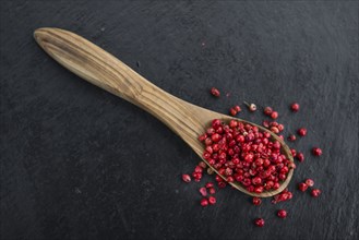 Portion of Pink Peppercorns as detailed close up shot on a slate slab, selective focus