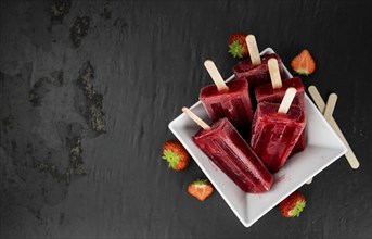 Slate slab with homemade Strawberry Popsicles (selective focus, close-up shot)