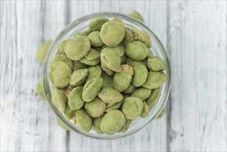 Wasabi coated Peanuts as high detailed close-up shot on a vintage wooden table (selective focus)