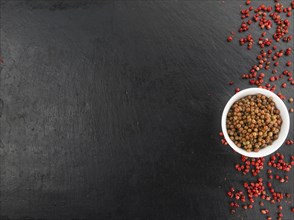 Some Pink Peppercorns (preserved) on a slate slab as detailed close-up shot, selective focus