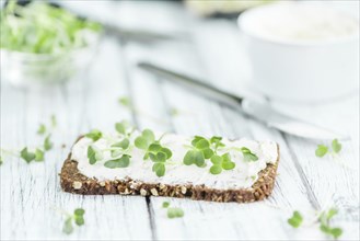 Slice of wholemeal bread with fresh cutted cress and cream cheese on an old wooden table (selective