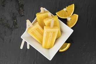 Some fresh made orange popsicles on a slate slab (selective focus, close-up shot)