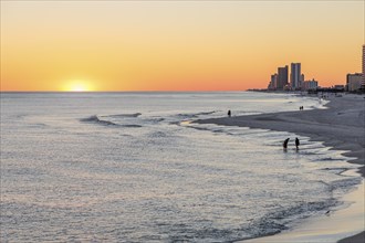 People walking and playing on the beach as the sun sets over the Gulf of Mexico at Gulf Shores,