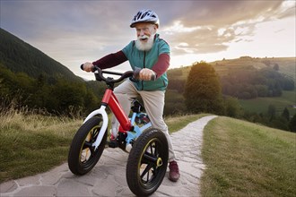 A man joyfully rides a red tricycle on a cobbled path through a picturesque landscape at sunrise,