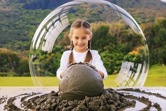 A smiling girl plays with a large clay ball in the middle of nature, with a transparent bubble