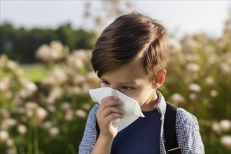 A little boy stands in a field holding a handkerchief to his nose because of an allergy, surrounded