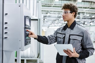 Factory worker in uniform operating a control panel in a factory environment, wearing safety