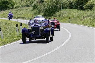 Blue vintage racing car leads a group of classic cars on a winding country road, classic car, car