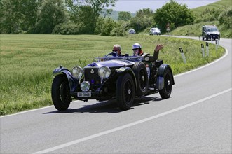 Black vintage car with two people on a country road during a rally. Passenger waving, classic car,