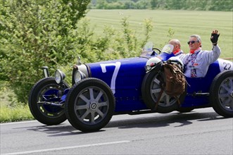 Blue vintage car with driver and co-driver on a country road during a rally. Driver waving, classic