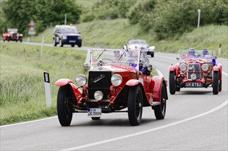 Racing car in a classic car rally on a winding country road, surrounded by green landscape, classic