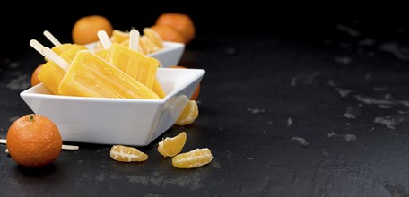 Homemade Tangerine Popsicles with some fresh fruits (close-up shot) on a vintage background