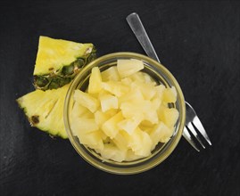 Portion of Preserved Pineapple (chopped) as detailed close up shot on a slate slab, selective focus