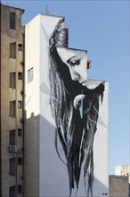 Woman with long hair looking at globe, mural in black and white by street artist INO, Athens,