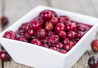 Old wooden table with fresh Preserved Cranberries (close-up shot, selective focus)