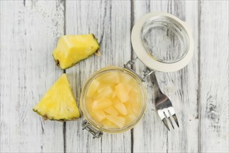 Chopped Pineapple (preserved) as high detailed close-up shot on a vintage wooden table, selective