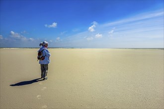 Elderly woman standing alone against the sun on the beach, North Sea, St. Peter Ording, Schleswig